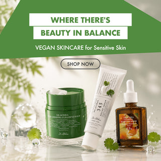 Three Dr. Althea vegan skincare products arranged on a reflective surface with green leaves and water droplets: a green jar of detoxing cleansing balm, a white tube of sensitive skin repair cream